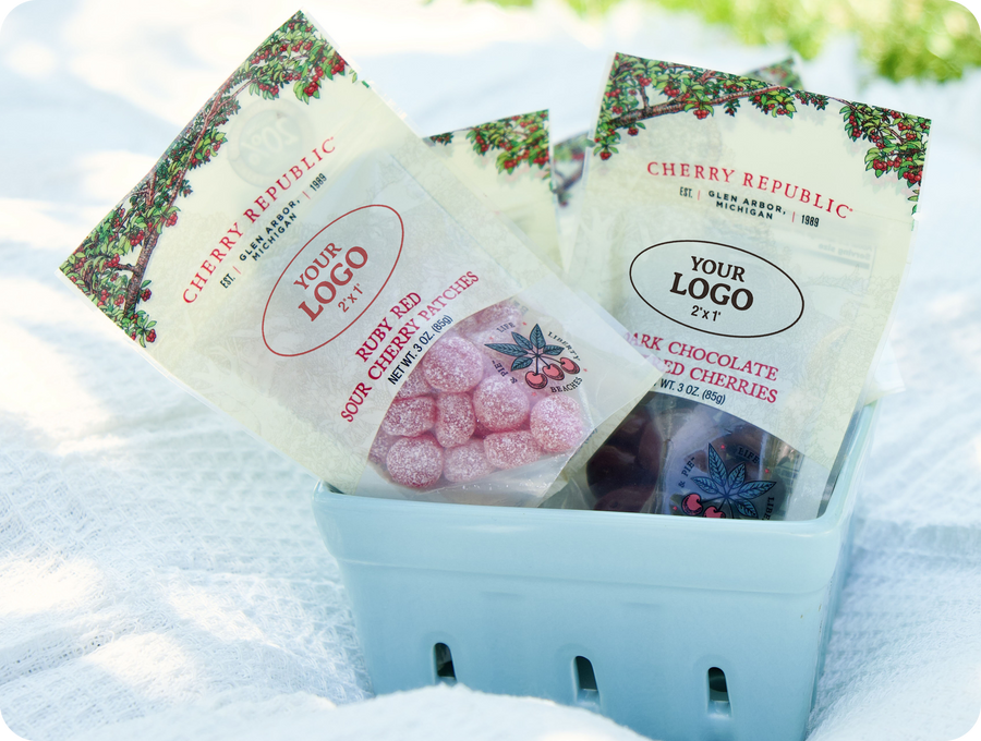 Two custom-labeled Cherry Republic 3 oz pouches in a berry basket on a picnic blanket