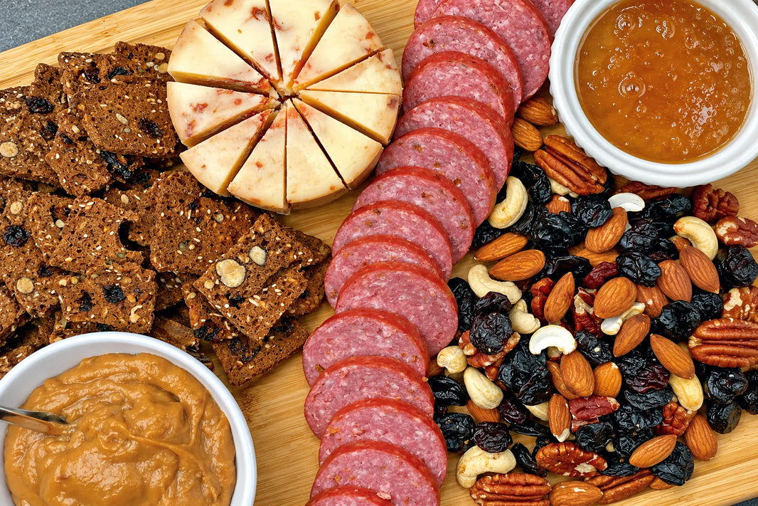 Cherry charcuterie board with sliced summer sausage, cherry white cheddar wedges, cherry nut mix, seeded crackers, and dips in small bowls