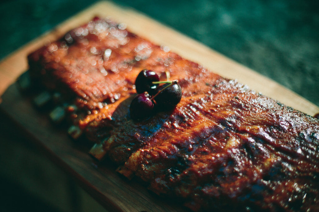 Grilled ribs served on a wooden board with a side of tangy cherry BBQ sauce for dipping