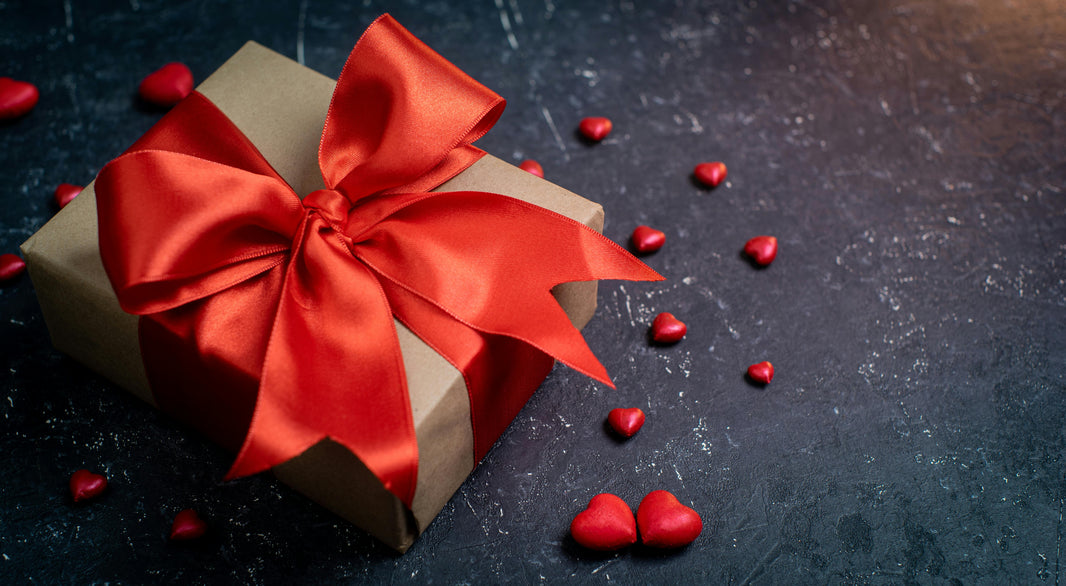 A Valentine’s gift box wrapped in brown paper with a bright red ribbon on a dark surface