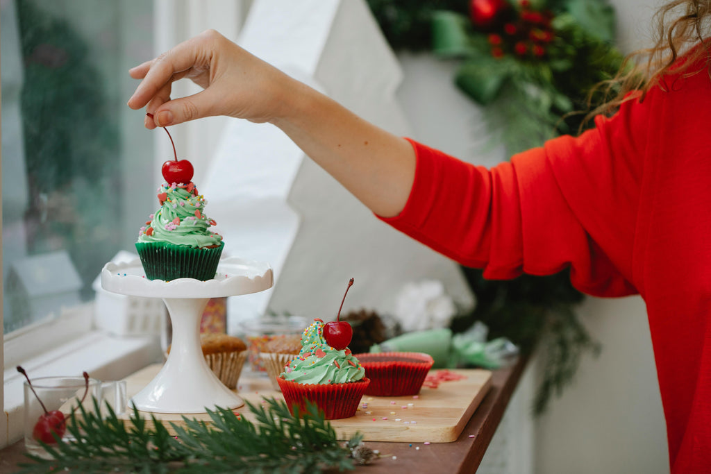 A woman placing a cherry on top of a cupcake Christmas dessert