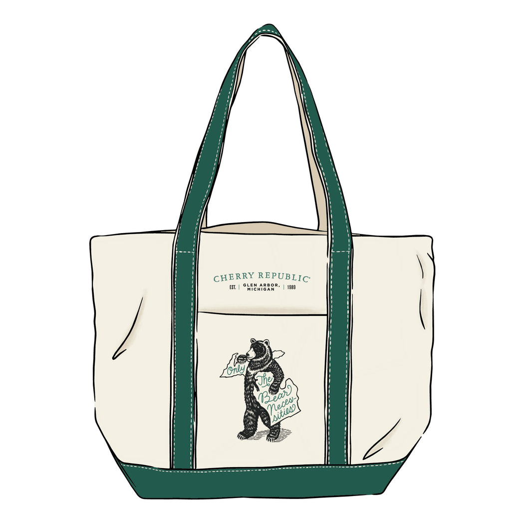 An off-white canvas tote bag with dark green handles, bottom trim, and piping, featuring a front pocket printed with 'CHERRY REPUBLIC' and an illustration of a bear holding a sign that reads 'Only The Bear Necessities'.