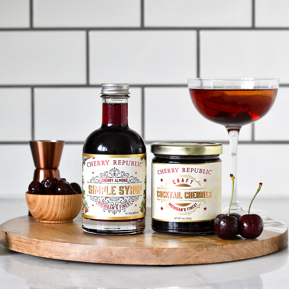 Bottles of cherry hour bundle products with a glass of cocktail and fresh cherries