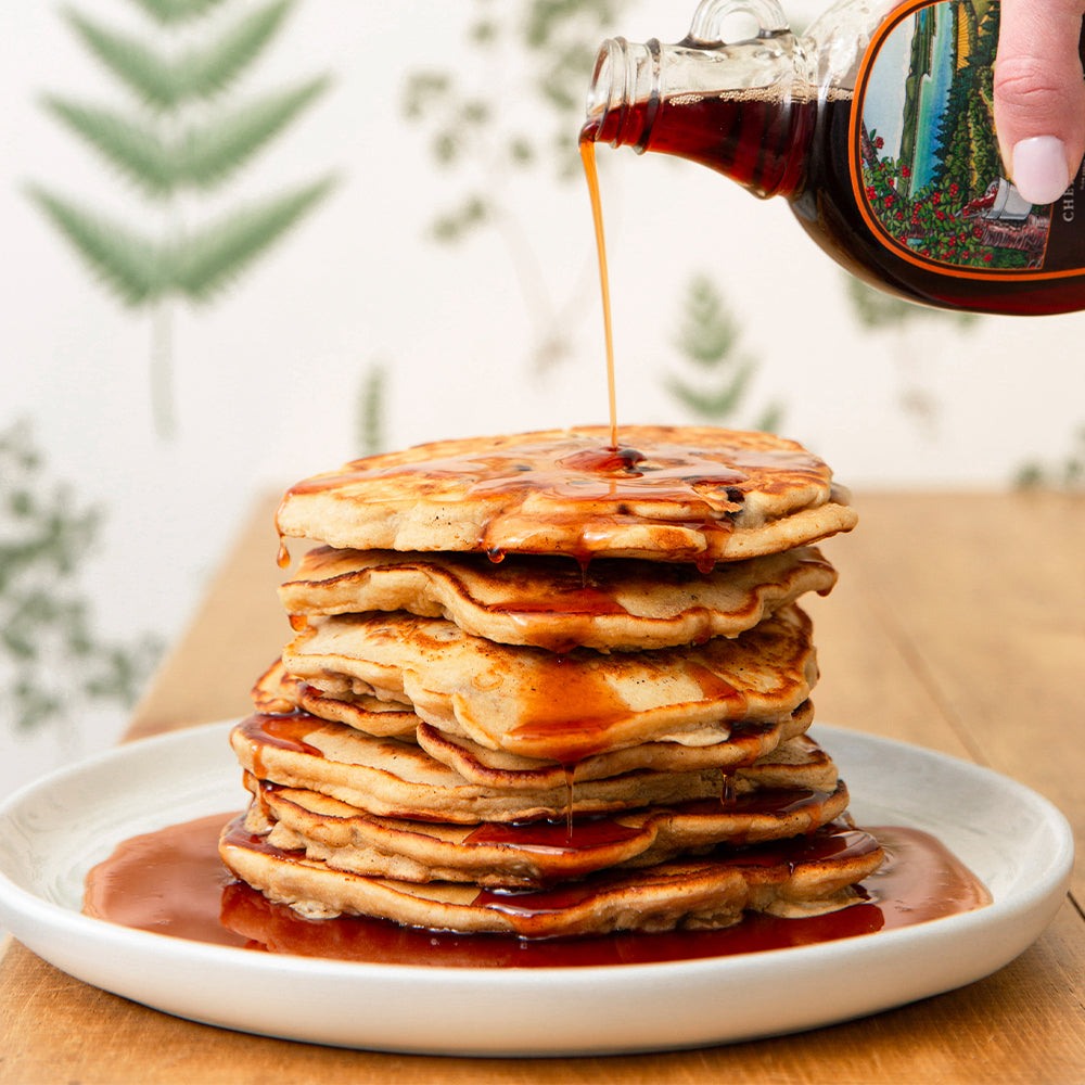 Maple syrup being poured over a stack of pancakes