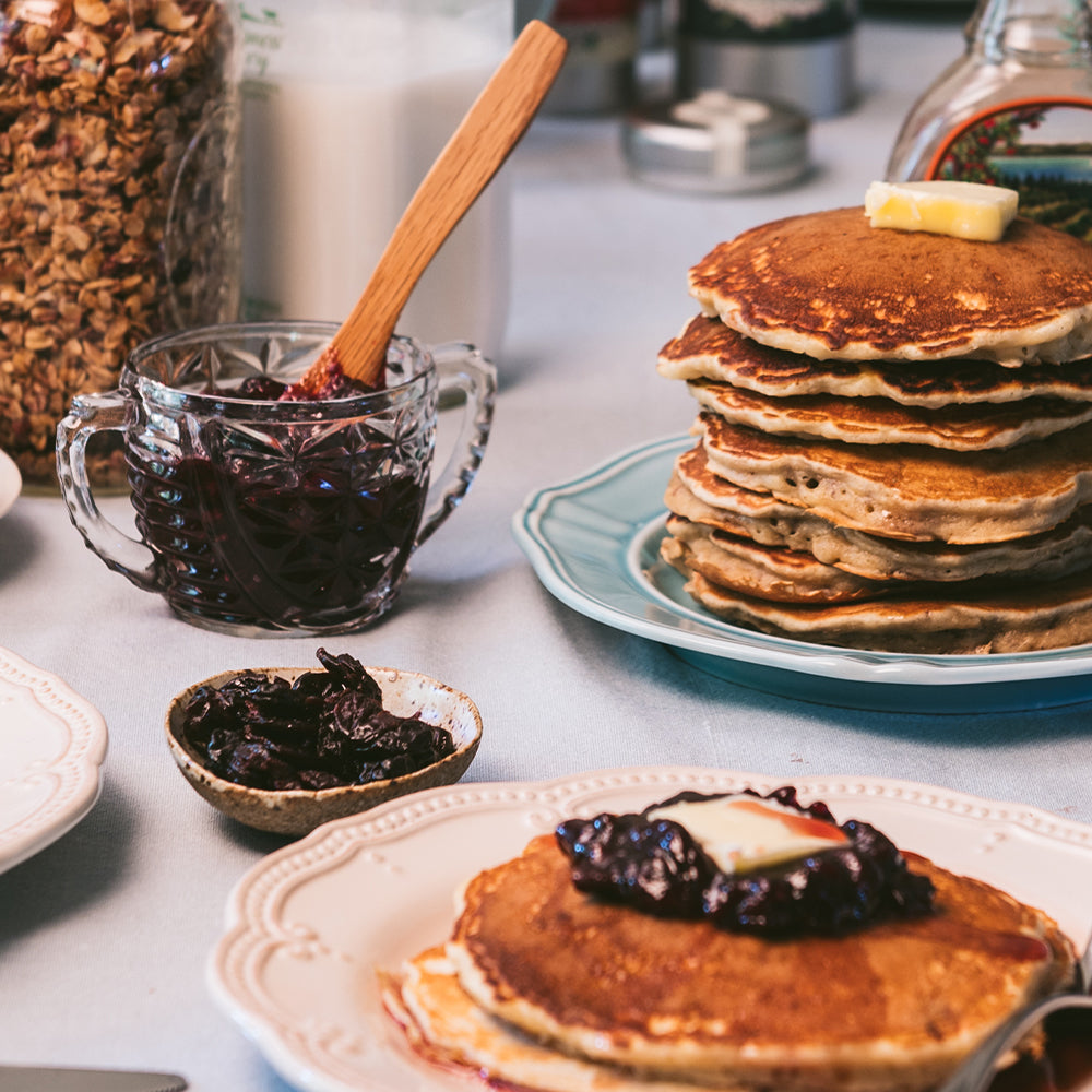 A stack of pancakes topped with cherry jam and syrup on a table